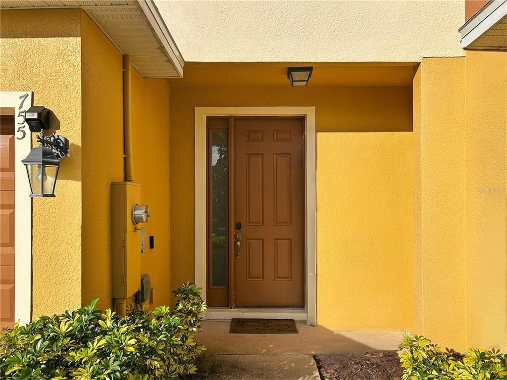The exterior view shows a yellow stucco wall with a brown front door and lantern — 755 MAROTTA LOOP, OCOEE, FL