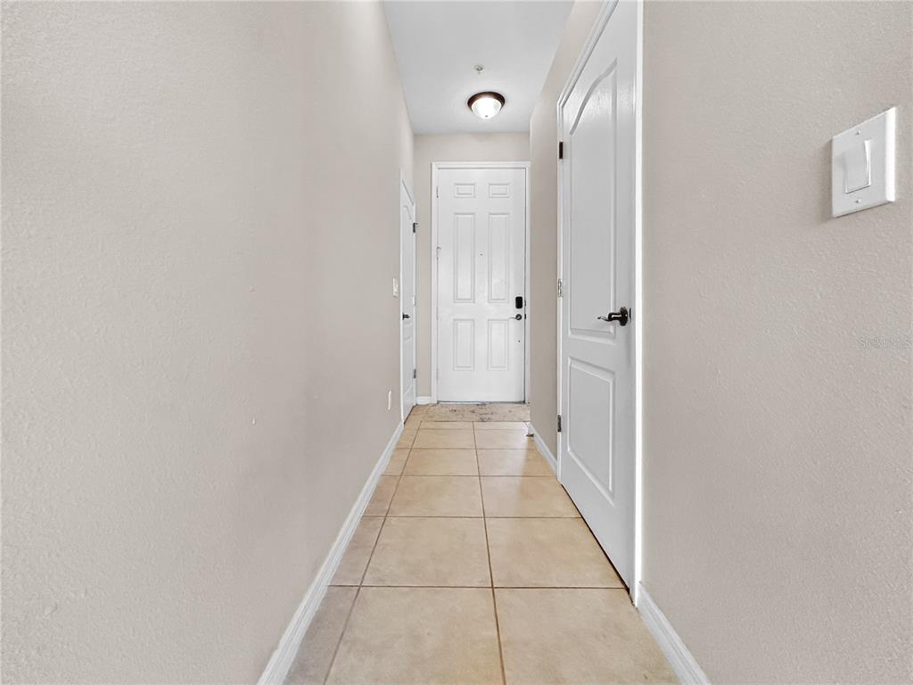 A narrow hallway with beige tile flooring leads to a white front door — 755 MAROTTA LOOP, OCOEE, FL