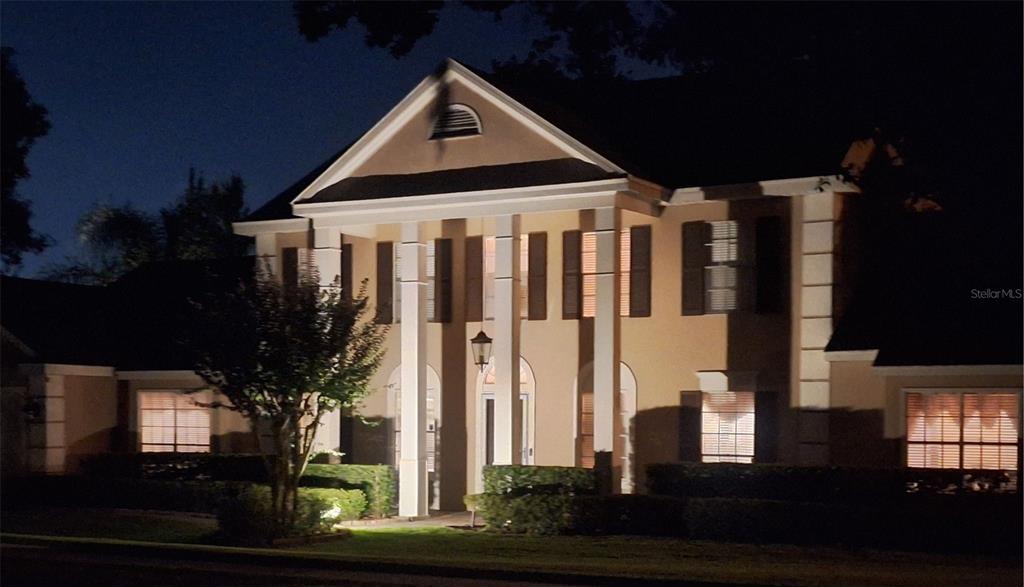 A two-story house with a columned portico and shutters is illuminated at night — 236 S SHADOWBAY BOULEVARD, LONGWOOD, FL