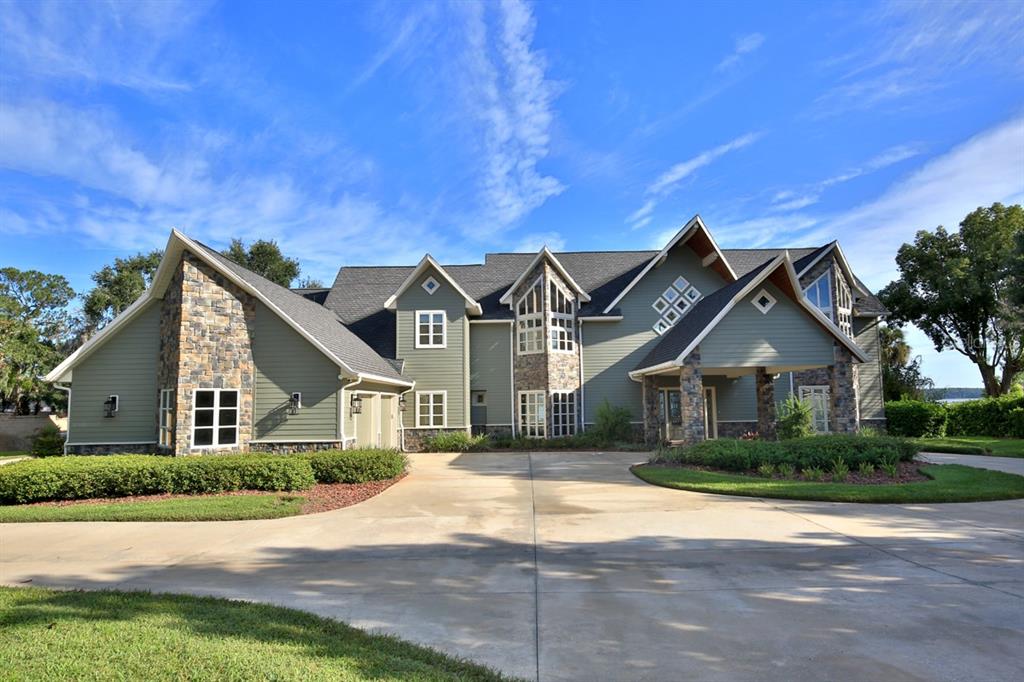 A large, multi-story house with green siding, stone accents, and a paved driveway — 11035 SE SUNSET HARBOR ROAD, SUMMERFIELD, FL