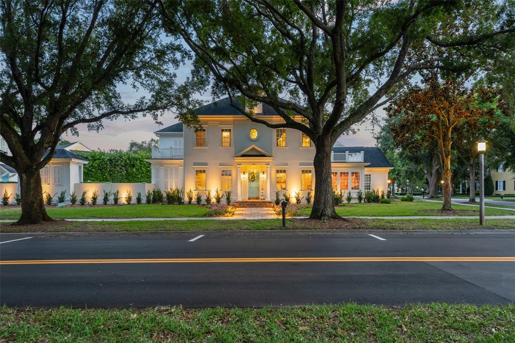 A two-story white house with a symmetrical facade, lit windows, and large trees in front — 706 GOLFPARK DRIVE, CELEBRATION, FL