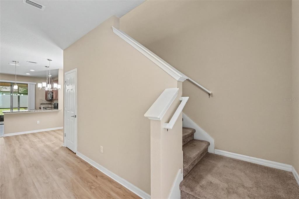 A carpeted staircase with a white handrail sits beside a doorway and a kitchen area — 5117 LEVANA STREET, PALMETTO, FL