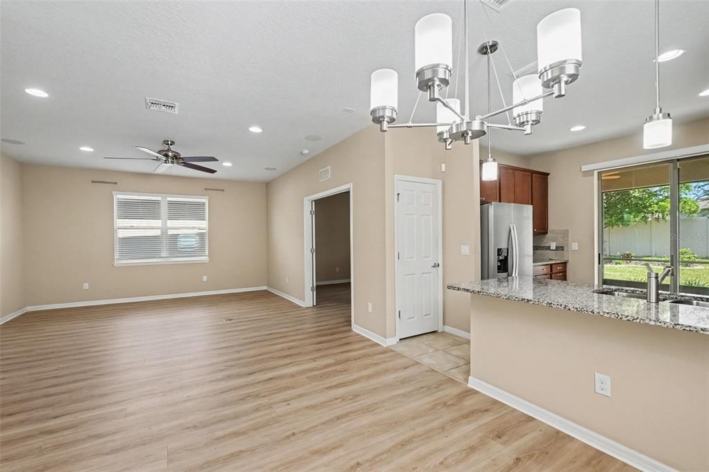A kitchen with granite countertops overlooks an open-concept living area with light wood-look flooring — 5117 LEVANA STREET, PALMETTO, FL