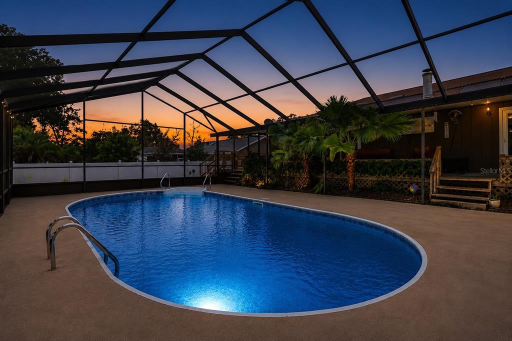A swimming pool enclosed by a screened lanai at sunset with a wooden deck nearby — 3265 NE 30 COURT, OCALA, FL