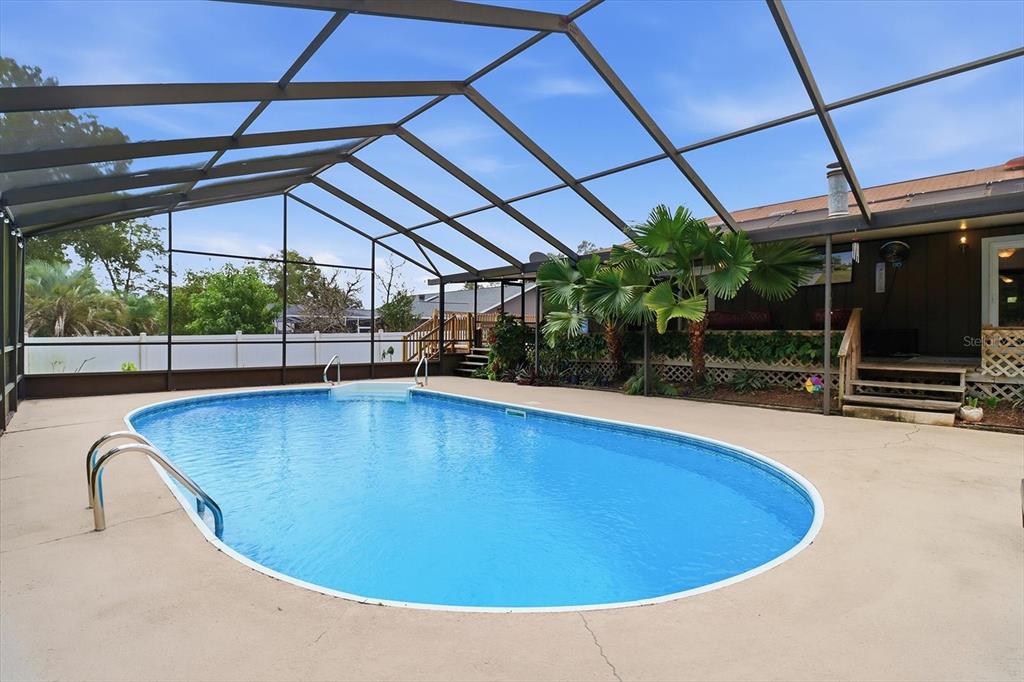An outdoor swimming pool is enclosed by a screened-in lanai next to a house — 3265 NE 30 COURT, OCALA, FL