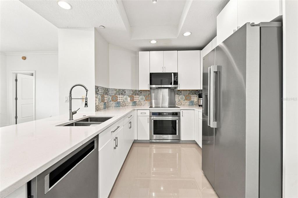 A modern kitchen features white cabinets, stainless steel appliances, and a patterned tile backsplash — 1209 E CUMBERLAND AVENUE UNIT 608, TAMPA, FL