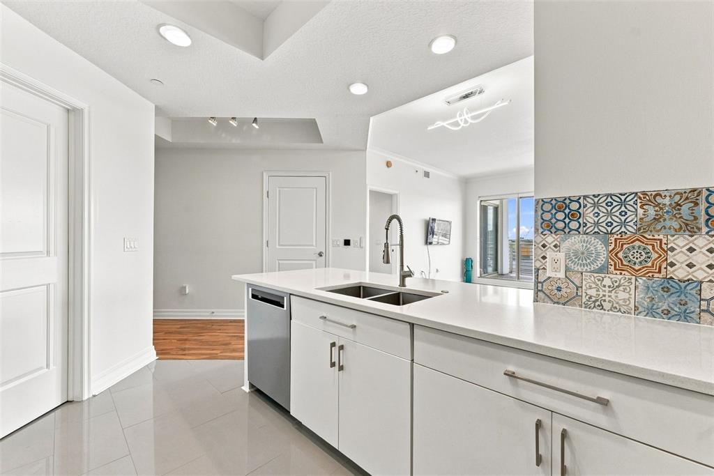 A modern kitchen features white cabinetry, a stainless steel dishwasher, and a patterned tile backsplash — 1209 E CUMBERLAND AVENUE UNIT 608, TAMPA, FL