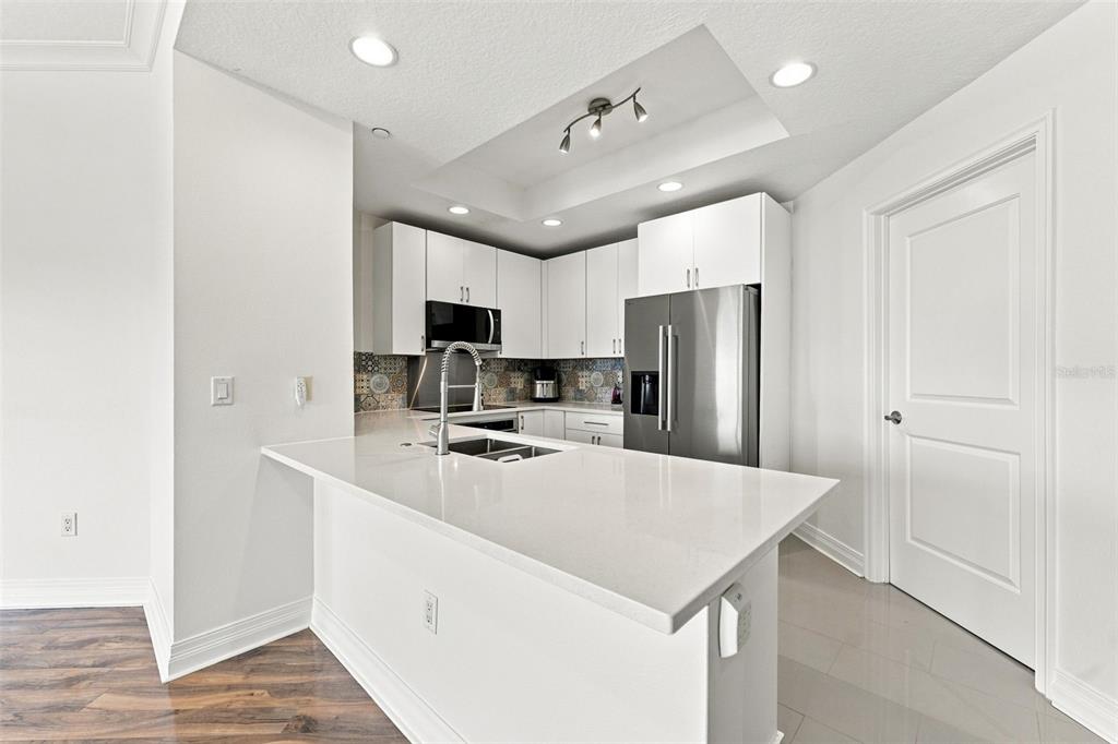 A kitchen features white cabinets, stainless steel appliances, and a white quartz peninsula countertop — 1209 E CUMBERLAND AVENUE UNIT 608, TAMPA, FL
