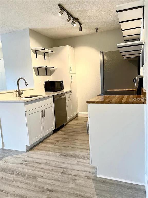 A kitchen features white cabinets, wood countertops, open shelving, and light-colored wood-look flooring — 10263 GANDY BOULEVARD N UNIT 311, ST PETERSBURG, FL