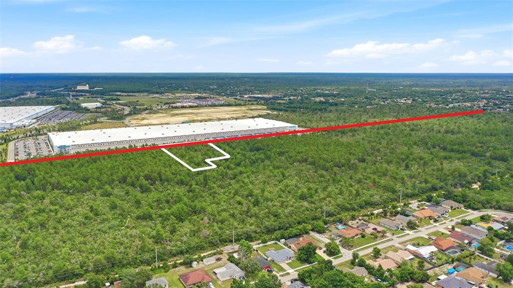 An aerial view shows a large warehouse bordering a wooded lot with a residential neighborhood — AMELIA (PAPER) AVENUE, DELTONA, FL