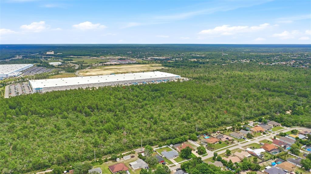 An aerial view shows a large warehouse facility situated behind a residential neighborhood and forest — AMELIA (PAPER) AVENUE, DELTONA, FL