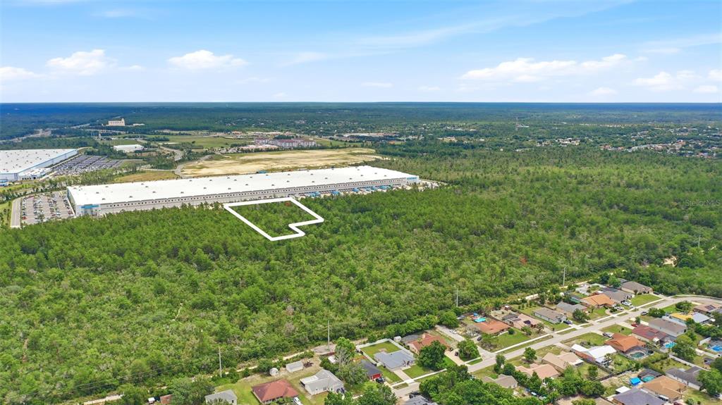 An aerial view shows a wooded lot outlined in white adjacent to a large warehouse — AMELIA (PAPER) AVENUE, DELTONA, FL