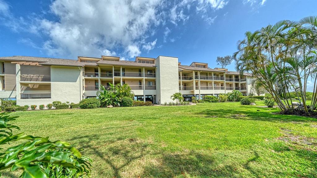 A multi-story apartment building with balconies sits behind a large, grassy lawn — 3840 MARINERS WAY UNIT 524A, CORTEZ, FL