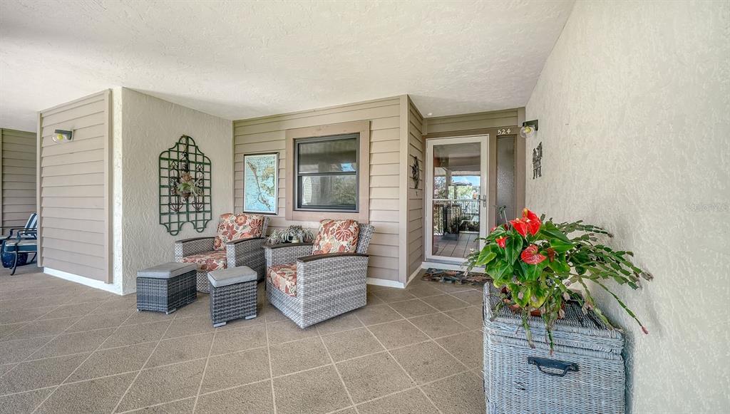 A covered patio features wicker chairs, ottomans, a potted plant, and a glass-paneled front door — 3840 MARINERS WAY UNIT 524A, CORTEZ, FL
