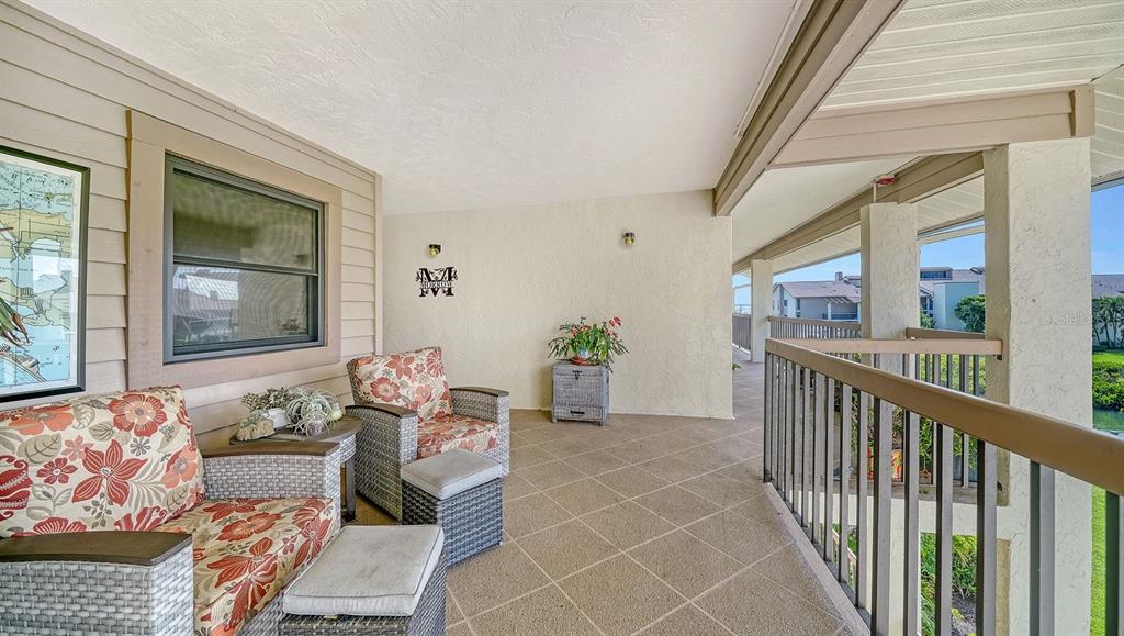 A covered balcony features tiled flooring, wicker furniture with floral cushions, and a metal railing — 3840 MARINERS WAY UNIT 524A, CORTEZ, FL
