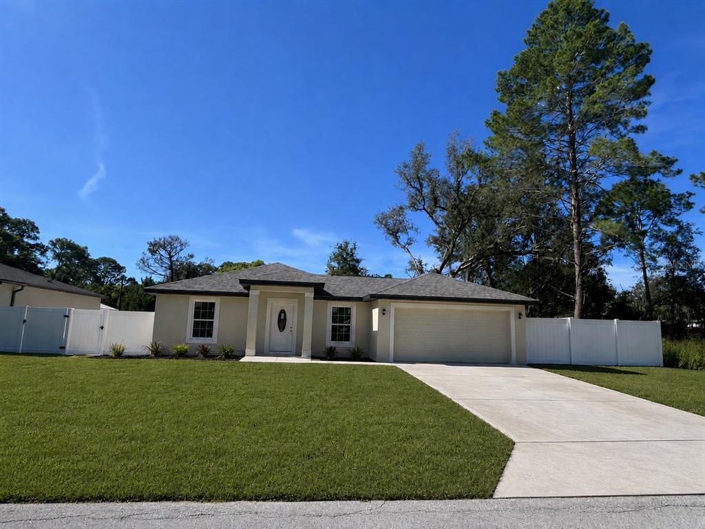 A single-story house with a beige exterior, a two-car garage, and a white vinyl fence — 7358 CENTERWOOD AVENUE, SPRING HILL, FL