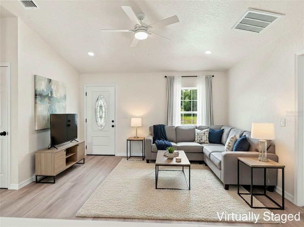 A living room features a gray sectional sofa, a television on a console, and light flooring — 7358 CENTERWOOD AVENUE, SPRING HILL, FL