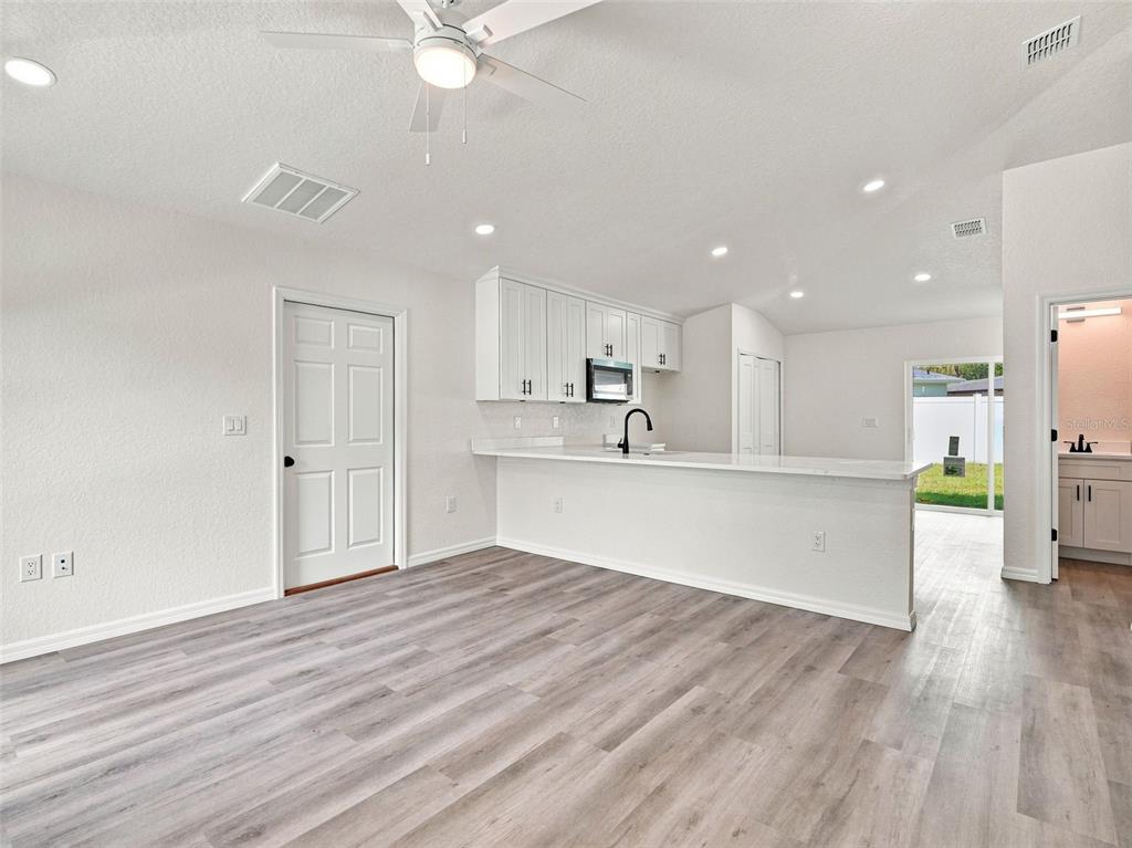 A bright kitchen with white cabinets and a breakfast bar overlooks a living area — 7358 CENTERWOOD AVENUE, SPRING HILL, FL