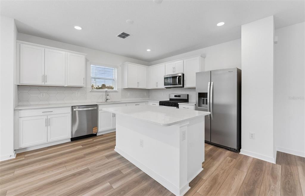 A modern kitchen features white cabinets, stainless steel appliances, a center island, and wood-look flooring — 9740 CRESCENT MOON DRIVE, RIVERVIEW, FL