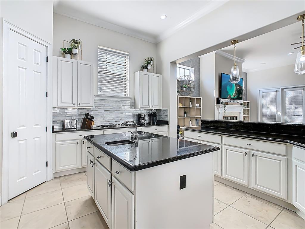 A kitchen features white cabinets, a black granite island, and tile flooring — 535 MUIRFIELD LOOP, REUNION, FL