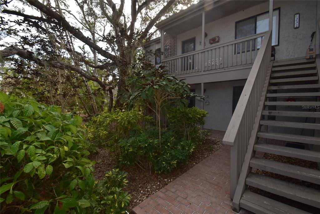 A two-story building exterior features a brick walkway, wooden stairs, and lush green landscaping — 1633 BOATHOUSE CIRCLE UNIT HA231, SARASOTA, FL