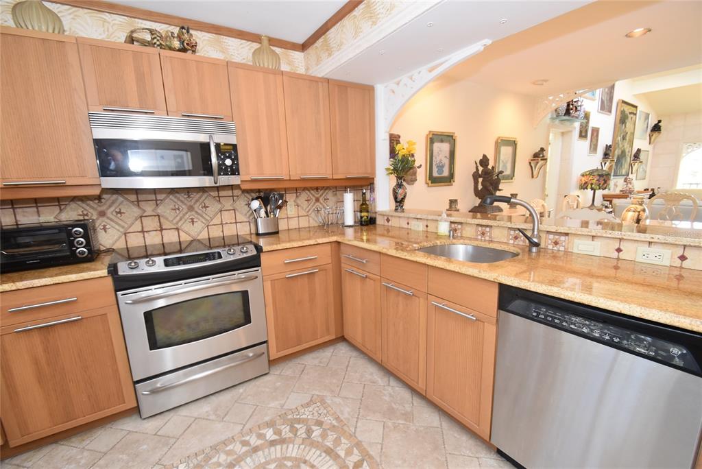 A kitchen features light wood cabinets, granite countertops, stainless steel appliances, and tiled flooring — 1633 BOATHOUSE CIRCLE UNIT HA231, SARASOTA, FL