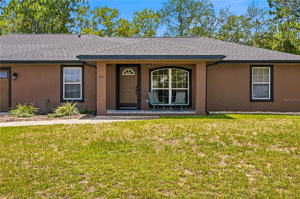 A single-story house with brown stucco walls, a covered entryway, and a front lawn — 24 FIR TRAIL PASS, OCALA, FL