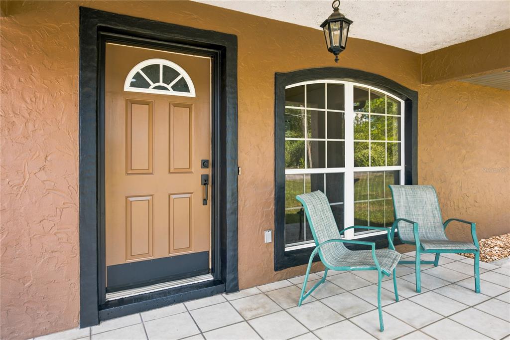 A covered porch features a brown front door, a large arched window, and two chairs — 24 FIR TRAIL PASS, OCALA, FL