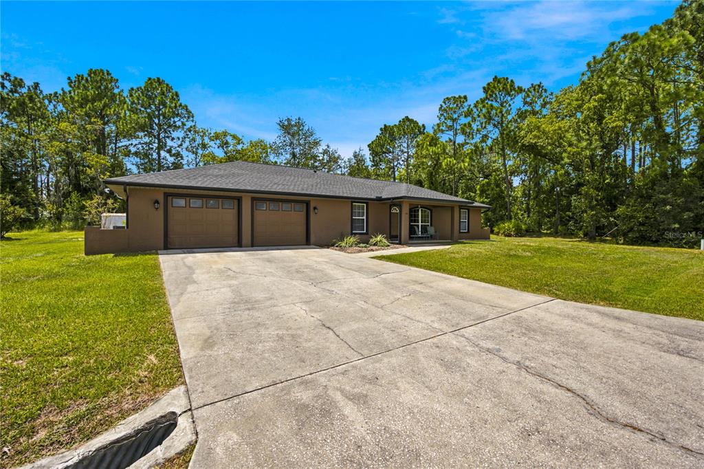 A single-story house with a two-car garage and a concrete driveway sits on a grassy lot — 24 FIR TRAIL PASS, OCALA, FL
