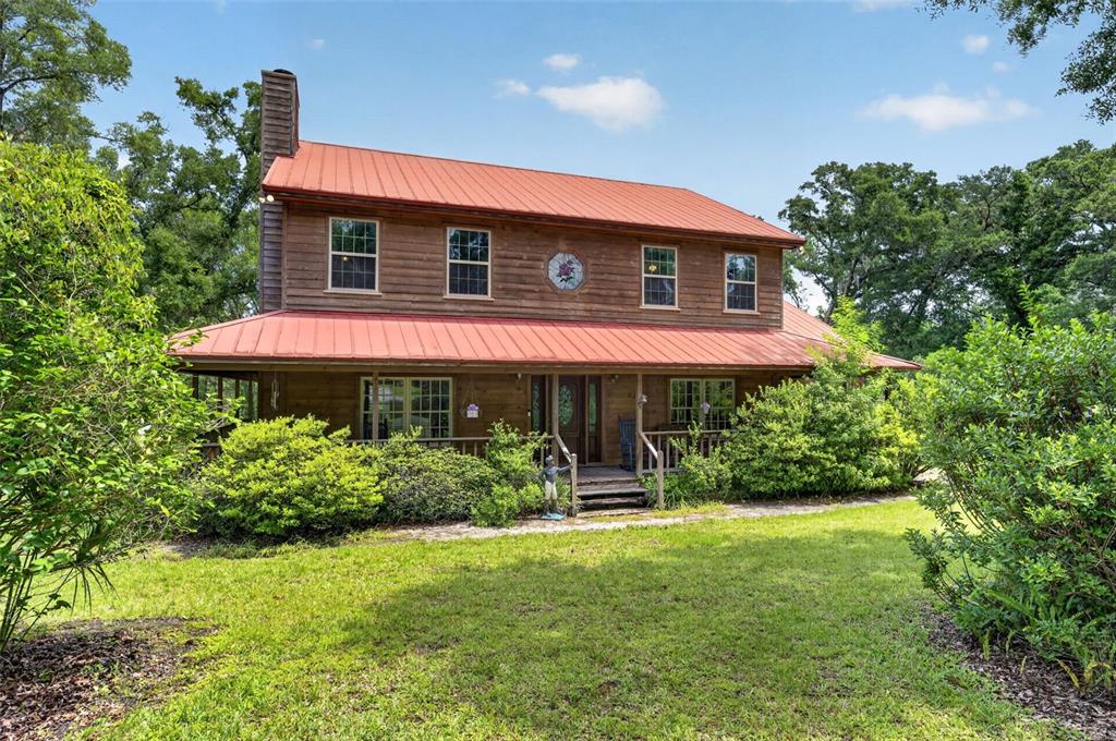 A two-story wooden house with a red metal roof and a wrap-around porch — 20621 SHADY OAK LANE, EUSTIS, FL