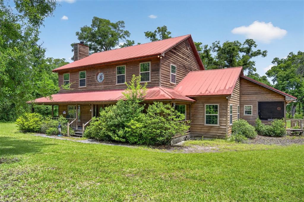 A two-story wooden house with a red metal roof and a wrap-around porch — 20621 SHADY OAK LANE, EUSTIS, FL