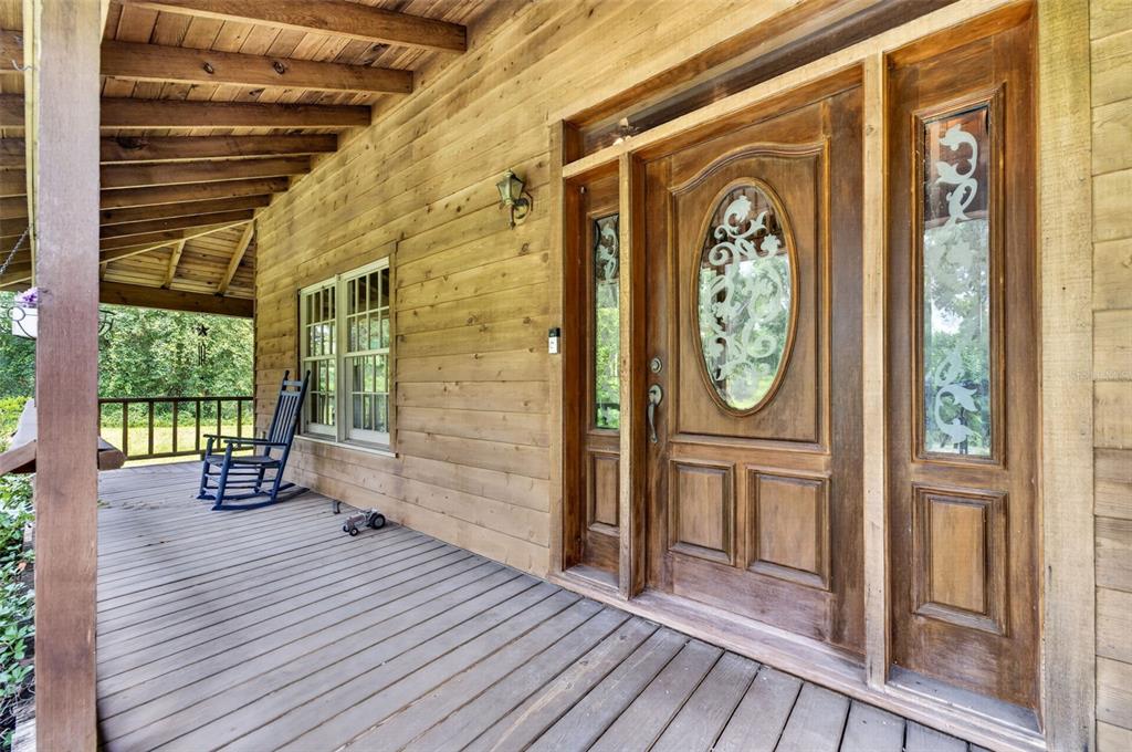 A wooden porch features a rocking chair, horizontal siding, and a decorative front door — 20621 SHADY OAK LANE, EUSTIS, FL