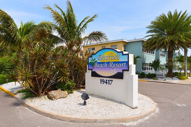 A sign for Barefoot Beach Resort stands in front of a multi-story building and palm trees — 19417 GULF BOULEVARD UNIT A-105, INDIAN SHORES, FL