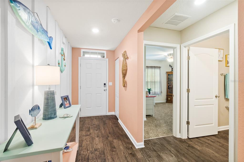 A bright entryway features wood-look flooring, a white front door, and coastal-themed wall decor — 1 RICHFIELD PLACE, PALM COAST, FL