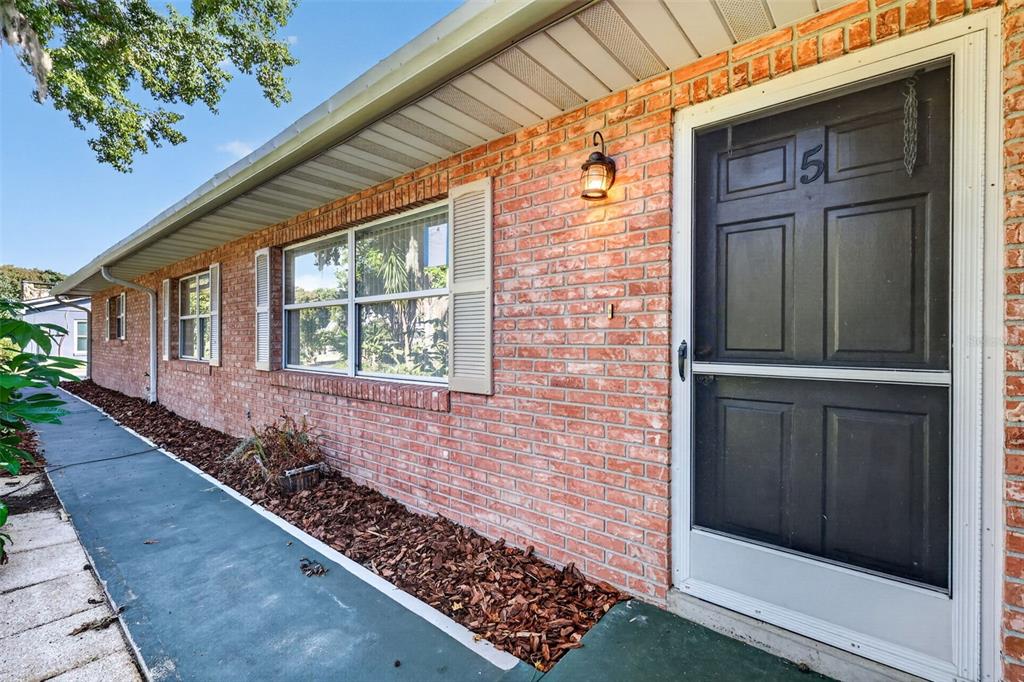 A brick exterior wall features a black front door, a window with shutters, and mulch — 5 HERMOSA DRIVE, EUSTIS, FL