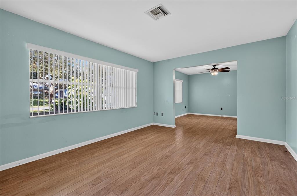 An empty room with light blue walls, wood-look flooring, and a large window with blinds — 5 HERMOSA DRIVE, EUSTIS, FL