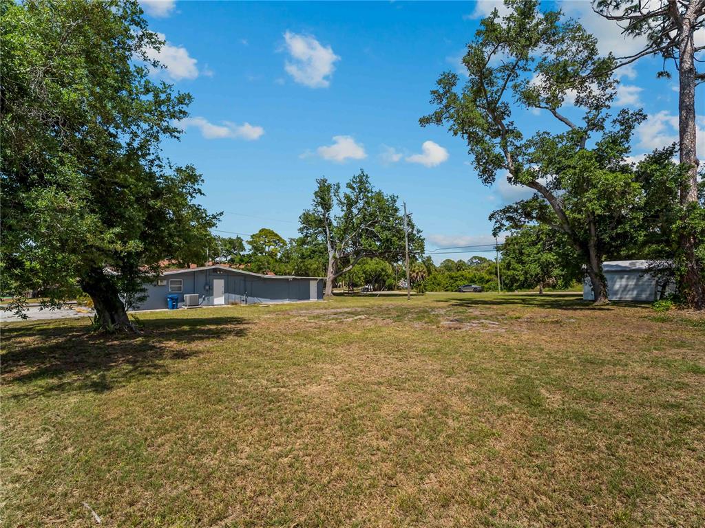 A grassy lot features a gray building, a small shed, and several large trees — SHAMROCK DRIVE, VENICE, FL