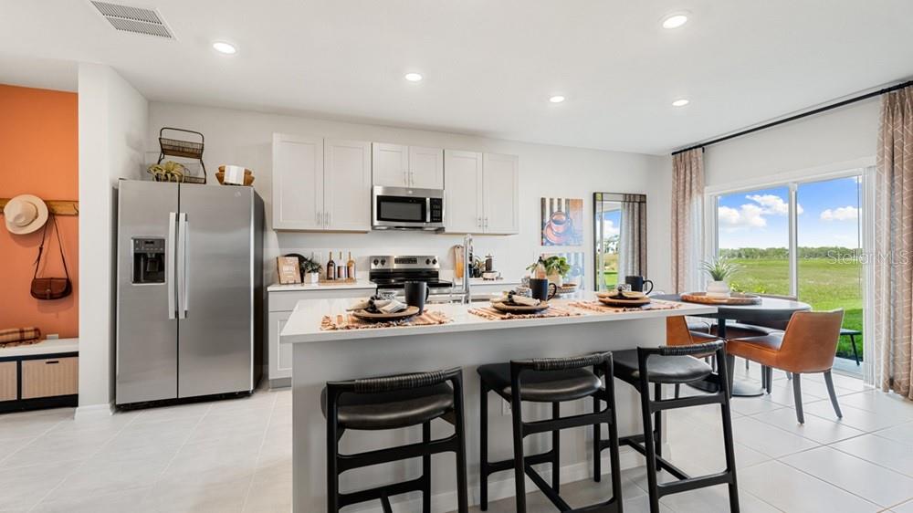 A modern kitchen features white cabinetry, stainless steel appliances, a central island, and dining area — 13827 SHELLMORE AVENUE, PALMETTO, FL