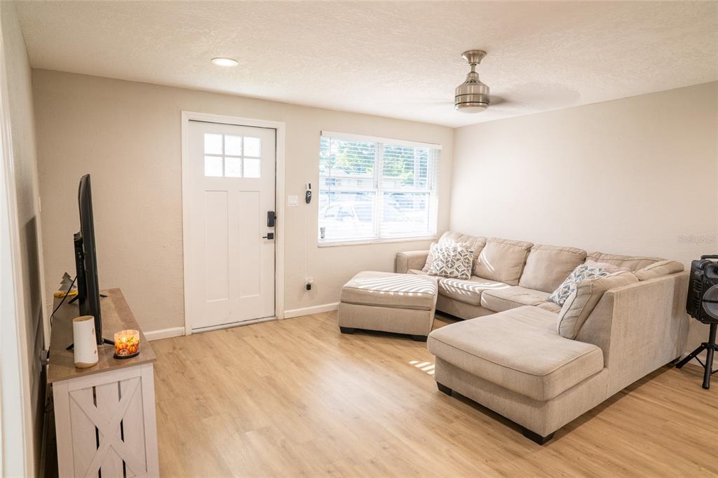 A living room features light wood-look flooring, a beige sectional sofa, and a white door — 11041 TAFT DRIVE, PORT RICHEY, FL