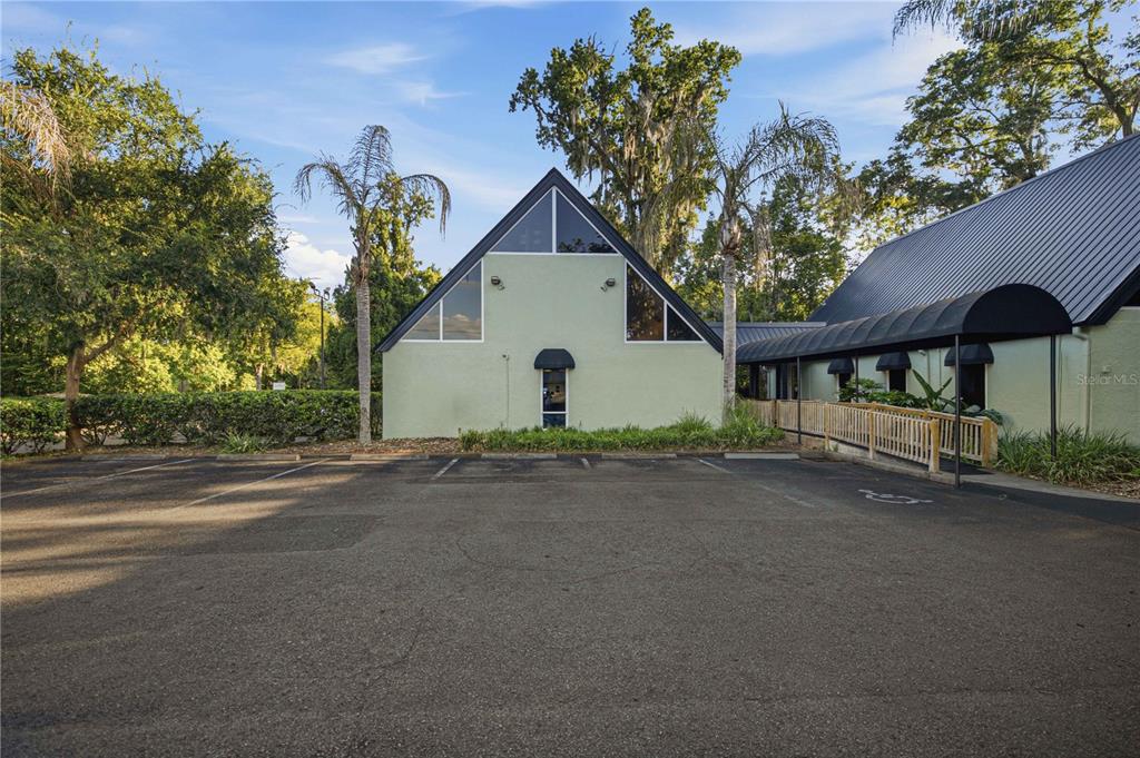 A parking lot sits in front of two connected buildings with A-frame roofs and trees — 2139 NE 2ND STREET UNIT B1, OCALA, FL
