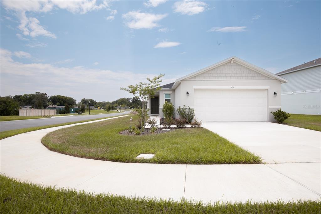 A single-story suburban house with a white garage, light-colored siding, and a curved concrete sidewalk — 9791 CARSON WAY, LEESBURG, FL