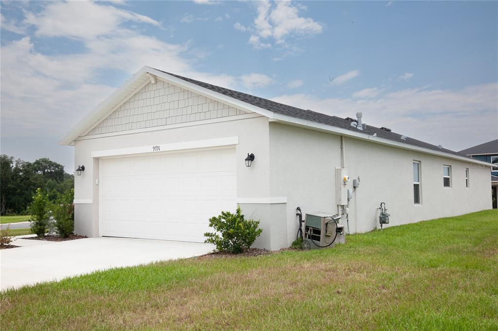 A side view of a single-story house exterior featuring a garage and a grassy lawn — 9791 CARSON WAY, LEESBURG, FL