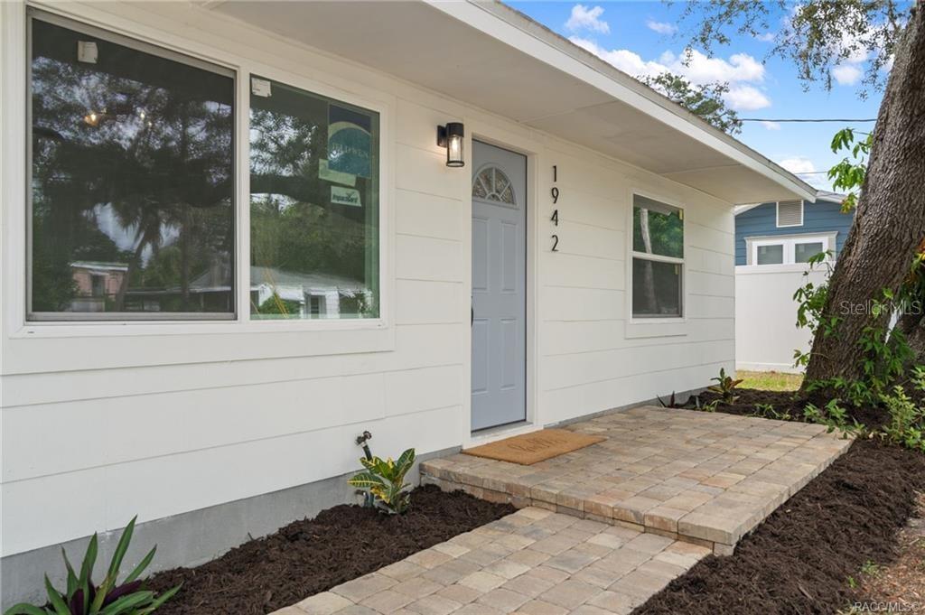 A white house exterior features a light blue front door, a paved walkway, and landscaping — 1942 SPRINGTIME AVENUE, CLEARWATER, FL