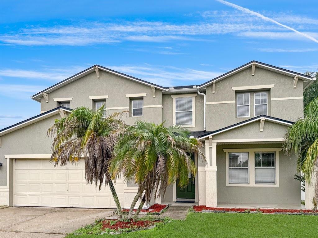 A two-story house with a beige stucco exterior, a two-car garage, and palm trees — 2024 BEARING LANE, KISSIMMEE, FL
