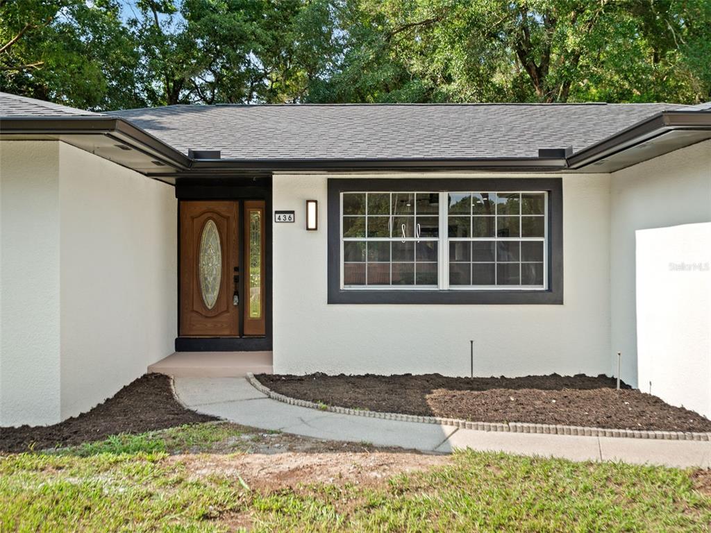 The exterior of a house features a white stucco facade, a dark-framed window, and a door — 436 BISON CIRCLE, APOPKA, FL