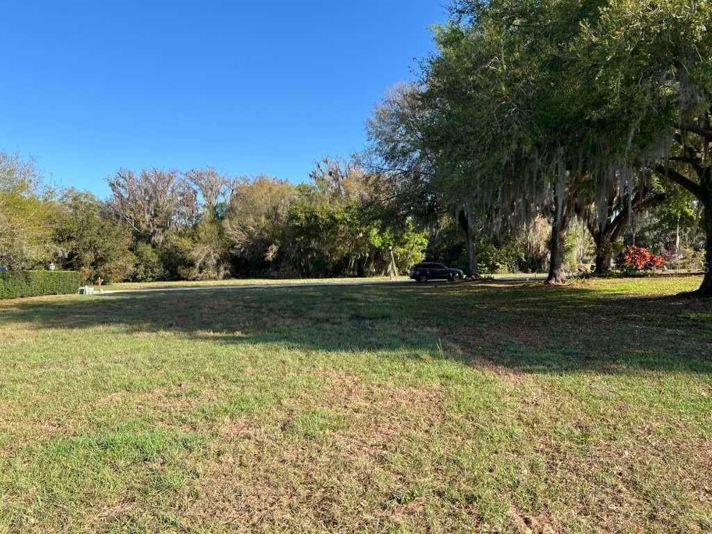 A grassy, open lot features large oak trees with Spanish moss and a parked vehicle — 6208 AQUAVISTA DRIVE, SEBRING, FL