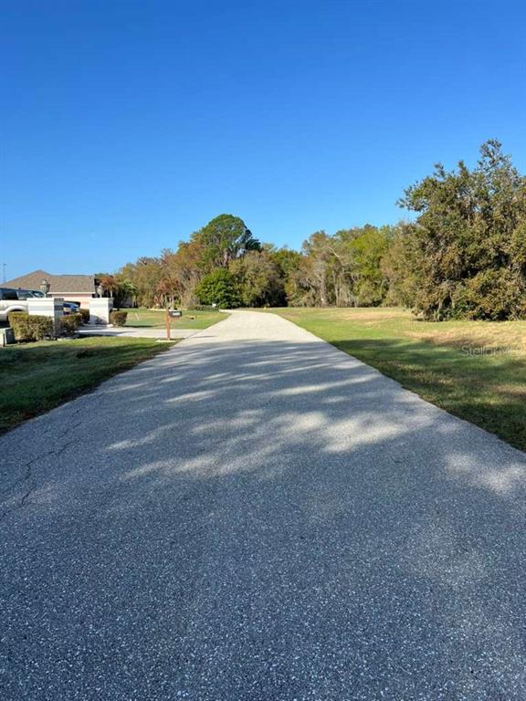 A paved driveway leads toward a residential property with trees and a clear blue sky — 6208 AQUAVISTA DRIVE, SEBRING, FL