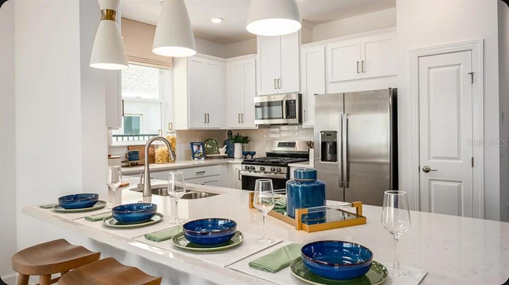 A kitchen features white cabinetry, stainless steel appliances, and a large island with blue place settings — 11234 SILVER TRUMPET LOOP, WINTER GARDEN, FL