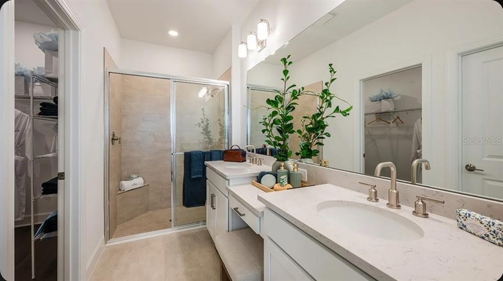 A bathroom features a glass-enclosed shower, dual vanity with white countertops, and an attached closet — 11234 SILVER TRUMPET LOOP, WINTER GARDEN, FL