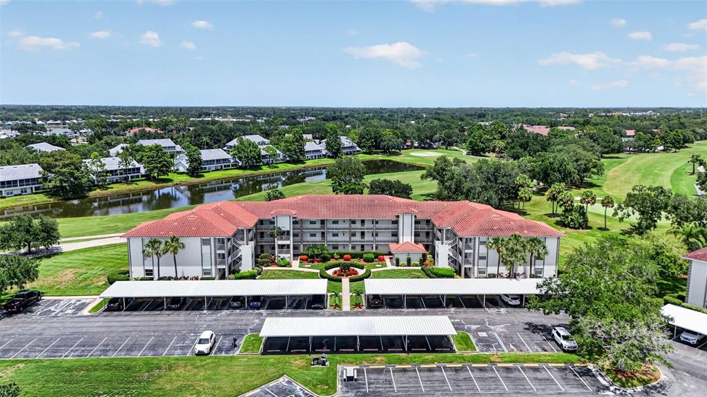 An aerial view shows a multi-story apartment building with a red tile roof and carports — 6505 STONE RIVER ROAD UNIT 308, BRADENTON, FL